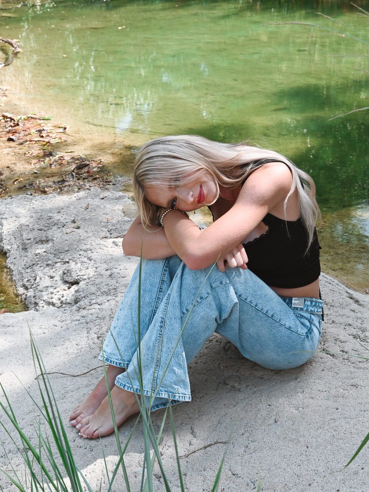 Senior portrait crouched on a creekside rock in warm summer light